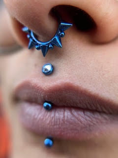 Composição de piercings azuis no nariz e lábios — trabalho de Thaís Muniz